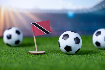 Small Trinidad and Tobago flag and soccer balls positioned on lush green turf, symbolizing national football passion, global sports event, and team competition spirit