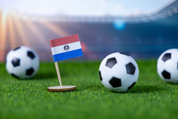 Small Paraguay flag stands proudly on green artificial turf with miniature soccer balls, symbolizing global football competition and national team spirit