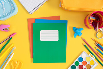 Back to school background. Colorful assortment of school stationery on bright yellow background, stack of notebooks, pencil case, pens, pencils, watercolor paints and more.