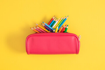 Back to school theme with pencil case full of pencils on bright yellow background, school supplies. Top view