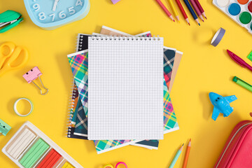 Flat lay with colorful school stationery and notebook on yellow background, top view. Back to...