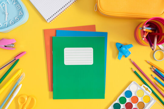 Back to school background. Colorful assortment of school stationery on bright yellow background, stack of notebooks, pencil case, pens, pencils, watercolor paints and more.