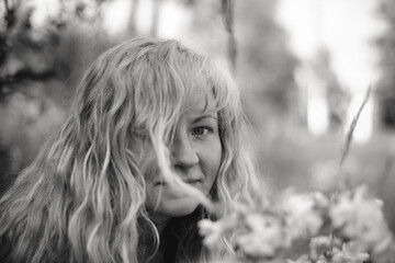 A black-and-white close-up portrait of a woman standing in a field, her light hair gently moving...