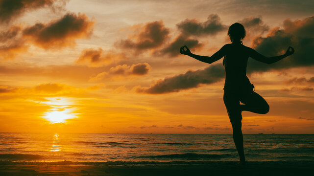 The silhouette of a woman practicing yoga on the beach during a breathtaking sunset. Her pose is steady and graceful, framed by glowing skies and the rhythm of the sea.