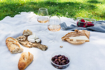 Two glasses of rose wine with snacks on a blanket on the grass in the park. Summer picnic. Alcohol....