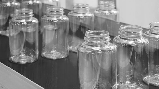 Empty plastic transparent bottles for pharmaceuticals, cosmetics and household chemicals stand in rows on an industrial conveyor belt at a factory.
