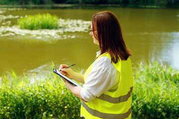 Female ecologist. Biologist is conducting research into the ecological state of nature near a body...