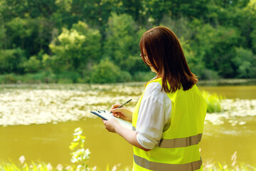 European female forestry inspector studies the condition of trees near water in a forest....