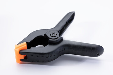 Obraz premium A black plastic clamp with an orange tip on a white background. The clamp is designed for holding objects securely in place. Ideal for DIY projects and crafts.