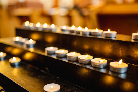 A row of tealight candles burns softly on a black metal stand, creating a peaceful and reflective ambiance often found in places of worship or memorials.
