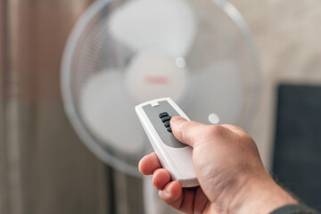 Man using remote control to turn on or off floor fan in room