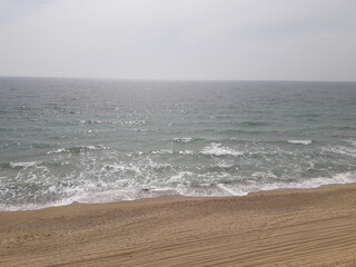 Empty sandy beach with sea waves under sunny sky
