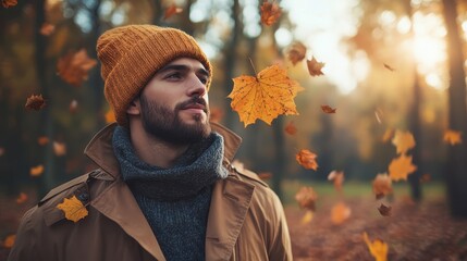 A young man wearing a cozy beanie and scarf stands in a forest as autumn leaves swirl around him, embodying tranquility and the beauty of nature's changing colors.