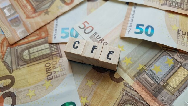 CFE acronym made of wooden letter cubes on pile of Euro banknotes. Cotisation Fonci&egrave;re des Entreprises (Business Property Tax)