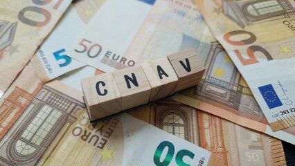 CNAV acronym made of wooden letter cubes on pile of Euro banknotes. Caisse Nationale d’Assurance...