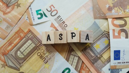 ASPA acronym made of wooden letter cubes on pile of Euro banknotes. Allocation de Solidarité aux...