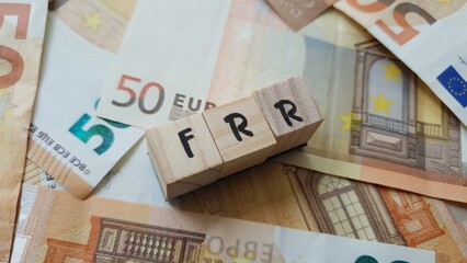 FRR acronym made of wooden letter cubes on pile of Euro banknotes. Fonds de Réserve pour les...