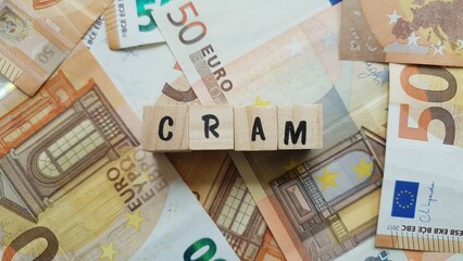 CRAM acronym made of wooden letter cubes on pile of Euro banknotes. Caisse Régionale d’Assurance...