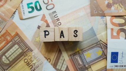 PAS acronym made of wooden letter cubes on pile of Euro banknotes. Prélèvement à la Source...