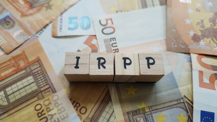 IRPP acronym made of wooden letter cubes on pile of Euro banknotes. Impôt sur le Revenu des...