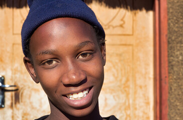 village single young african woman wearing a beanie standing in front of the house , in the yard, close portrait