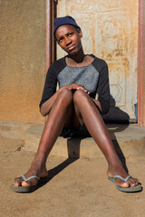 village single young african woman wearing a beanie standing in front of the house , in the yard, close portrait