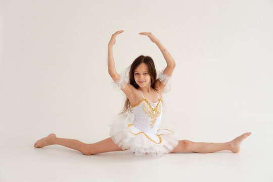 A ballerina girl dancing doing splits and stretching on white background in white tutu on white background. Girl doing ballet.