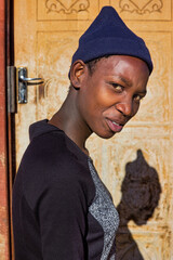 village single young african woman wearing a beanie standing in front of the house , in the yard, close portrait