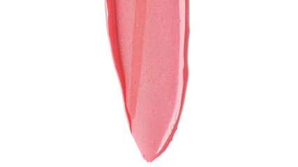 Fototapeta premium Glossy liquid makeup smear in a pinkish coral hue, showcasing texture and light reflecting on a white surface, shot with sharp focus.