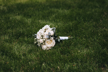 A beautiful wedding bouquet of flowers, white roses, lies on the green grass.