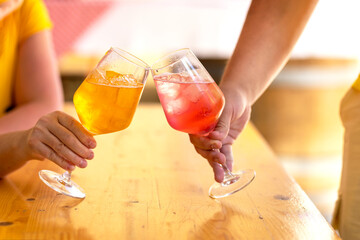 Glasses of pink and yellow alcoholic drink Aperol Spritz with ice on table on warm day. Celebration with glasses of refreshing fruity soft drink