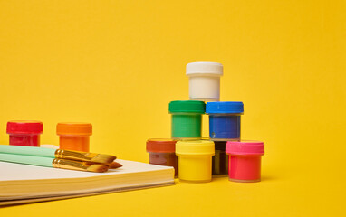 White spiral notebook, brushes and colorful paint cans symbolizing art