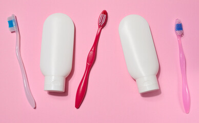 Three toothbrushes and two white plastic tubes of toothpaste placed on a pink background.