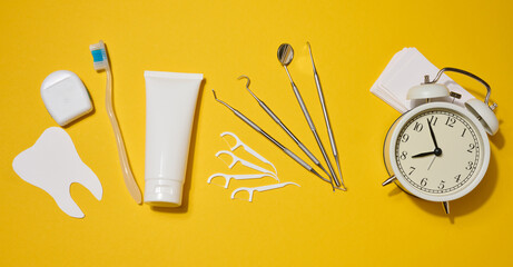 Dental floss in a case, white tube of toothpaste, dental instruments, plastic flossers, white alarm...