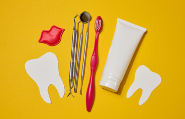 Red toothbrush, white tube of toothpaste, red decorative lips, dental instruments, dental floss in...