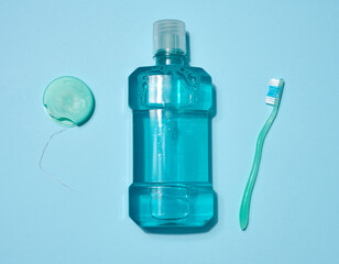 Bottle of blue mouthwash, dental floss in a blue case and green toothbrush placed on a blue...