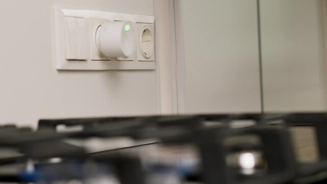 Hand Installing a Compact Gas Detector into Wall Socket Near Kitchen Stove for Safety Monitoring