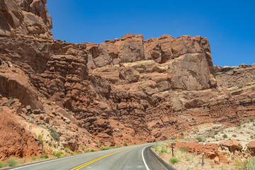 Winding road under tall rock cliffs in the Arches National Park in Moab, Utah. No people.