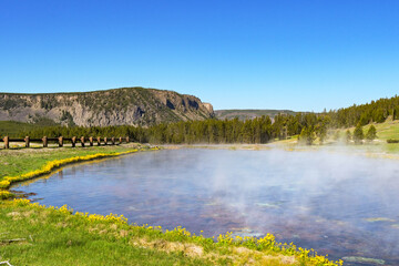 Scenic landscape view of a small lake of steaming boiling water in the geothermal area of the Terrace Springs in Yellowstone National Park. No people.