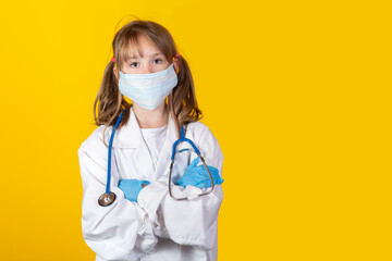 Cute little european blonde girl in adult doctor coat uniform with stethoscope wearing rubber gloves and mask on yellow background. Her arms are crossed on chest