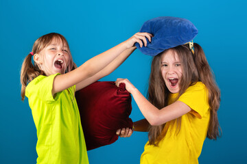Two young funny girls having pillow fight on blue background