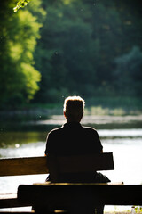 Man Sitting on Bench by Lake, Back View in Nature
