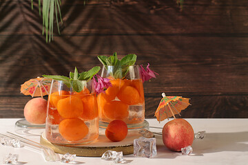 Iced peach tea or cocktail with mint and apricots, refreshing summer drink recipe. Two glasses with peach fruit lemonade on a rustic table, detox diet and weight loss concept, restaurant menu