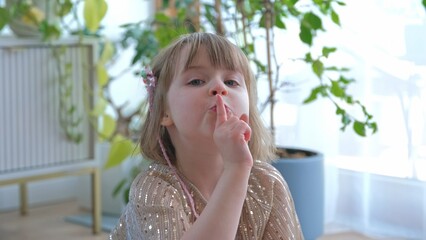 Adorable Happy Caucasian Preschooler Girl Making Shush Gesture Putting Index Finger on Her Lips and Making Funny Faces and Crossing Eyes