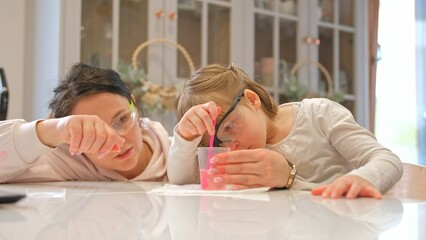 Caucasian Woman and Preschooler Daughter Child Girl Wearing Protective Glasses Having Fun Preparing STEM Science Experiment on Kitchen Table using Education Kit for Homeshooling Learning