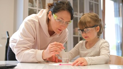 Caucasian Woman and Preschooler Daughter Child Girl Wearing Protective Glasses Having Fun Preparing STEM Science Experiment on Kitchen Table using Education Kit for Homeshooling Learning