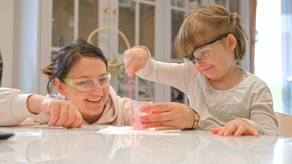 Caucasian Woman and Preschooler Daughter Child Girl Wearing Protective Glasses Having Fun Preparing STEM Science Experiment on Kitchen Table using Education Kit for Homeshooling Learning
