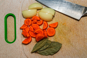 Chopped onion and carrot on a cutting board with bay leaf