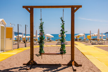 Decorative flower swings and empty beach loungers on a bright yellow path. Tranquil beach setup, summer rest and aesthetic vacation experience.