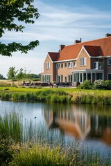 Obraz premium Bright summer day by a serene lake with a charming brick house reflecting on the water, surrounded by lush greenery in a peaceful countryside setting